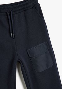 Dunkelnavy Sweatpants mit elastischem Bund, Kordelzug, Seitentaschen und einer strukturierten Stofftasche auf dem Oberschenkel.