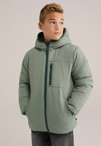 Zelena puhovka z zadrgo spredaj, velikim pokrovom, stranskimi žepi in žepom na prsih. Gladka tekstura, lahka zasnova in zaščitno polnilo.