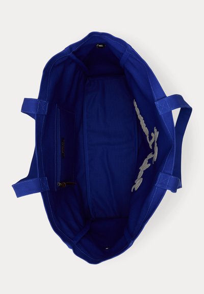 Τσάντα tote από βαμβακερό ύφασμα σε βαθύ μπλε χρώμα με διπλές λαβές, εσωτερική τσέπη με φερμουάρ και κεντημένο άσπρο κείμενο σε καλλιγραφία στην εσωτερική πλευρά.