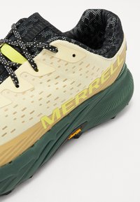 Krémová a zelená sportovní obuv s texturovaným svrškem, černými tkaničkami a výrazným žlutým brandingem "MERRELL" na boku.