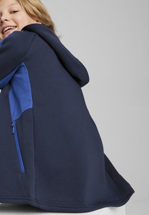 Sudadera azul marino con un panel texturizado azul, que presenta un bolsillo con cremallera en el lateral, fabricada en un tejido suave y con un dobladillo diseñado.