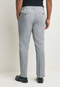 Pantaloni sartoriali grigi con motivo testurizzato, dotati di due tasche posteriori con bottoni, vestibilità slim e silhouette pulita e strutturata.