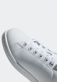 Baskets en cuir blanc avec bout rond, finition texturée, lacets plats et détails de coutures visibles. Semelle en caoutchouc avec léger soutien de la voûte plantaire.