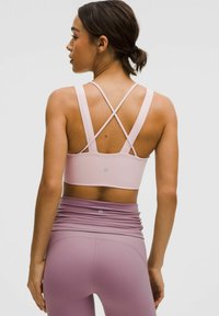 Jasnoróżowy stanik sportowy z krzyżującymi się ramiączkami, zestawiony z wysokim stanem lawendowymi legginsami z marszczonym detalem w pasie.