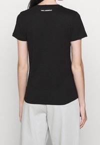 Camiseta de algodón negra de manga corta, con cuello redondo y un pequeño logo blanco en la parte superior de la espalda. Textura suave, diseño ajustado.