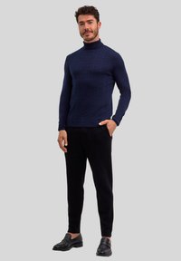 Granatowy sweter z golfem, dziany, z teksturowanym wzorem rybiej ości, w zestawie z czarnymi spodniami w kant i czarnymi loafersami.