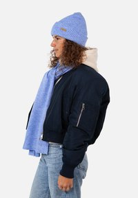 Giacca bomber della marina con polsini a coste, berretto a maglia blu chiaro e sciarpa coordinata. Tessuti texturizzati con dettagli della tasca con cerniera.