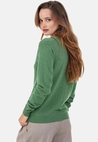 Pull vert en tricot à manches longues et col rond, avec un ourlet et des poignets côtelés, porté par-dessus un pantalon beige clair.