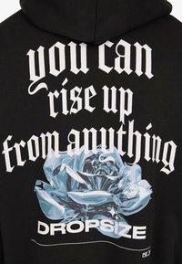 Felpa nera con testo gotico bianco "puoi rialzarti da qualsiasi cosa" sopra una rosa metallizzata blu e "DROPSIZE" in lettere grasse sotto.