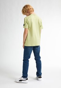 Lichtgroene shirt met korte mouwen en een ontspannen pasvorm, gecombineerd met blauwe denim jeans en witte sneakers met zwarte accenten.