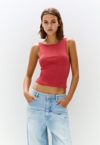 Top senza maniche aderente con scollo rotondo in tessuto rosso corallo, abbinato a jeans larghi a vita alta di colore blu chiaro con tasche frontali.