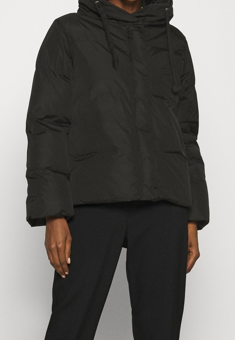 Svart puffjacka med hög krage, dragsko-huva och vida ärmar; har en slät, glänsande yta och minimala sömnadsdetaljer.