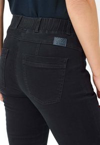 Pantalons en denim noir avec une taille élastique, dotés de deux poches arrière et d'une petite étiquette de marque ornée d'un motif étoilé.
