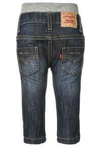 Vaqueros oscuros para toddler con una cinturilla elástica gris, que cuentan con bolsillos traseros con costuras amarillas y una etiqueta de la marca en la parte posterior.