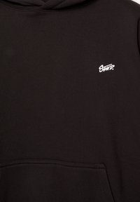 Sweat à capuche noir avec une poche kangourou à l’avant et un petit logo blanc "STWD." sur la partie supérieure gauche de la poitrine.