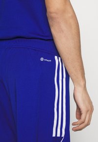 Pantalones cortos deportivos azules con rayas blancas a los lados, que presentan una cinturilla texturizada y un logo "AEROREADY" cerca del bolsillo trasero.