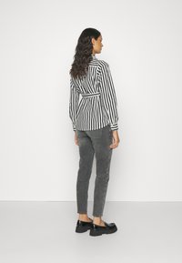 Bluză stripedă alb-negru cu o curea la talie, asortată cu pantaloni gri conici și pantofi cu platformă negri. Textură netedă, croială bine definită.