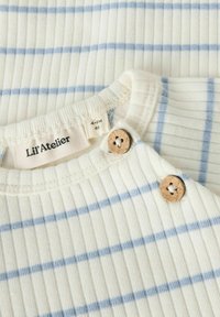 Chemise rayée pour bébé en tissu côtelé, avec des rayures bleu clair sur un fond crème, ornée de boutons en bois au niveau du col.