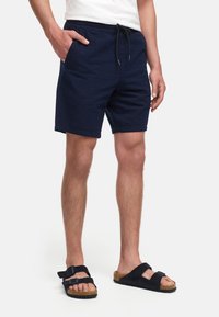 Granatowe szorty z teksturowanym splotem, elastyczną talią i sznurkiem. Noszone z czarnymi sandałami z podwójnymi paskami i korkową podeszwą.