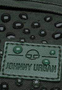 Tessuto verde con gocce d'acqua e superficie texturizzata, caratterizzato da un'etichetta verde rettangolare impressa con "JOHNNY URBAN."