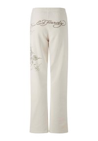 Pantaloni della tuta color crema con vestibilità rilassata. Presentano una grafica decorativa grigia e il logo "Ed Hardy" scritto in corsivo sul retro.