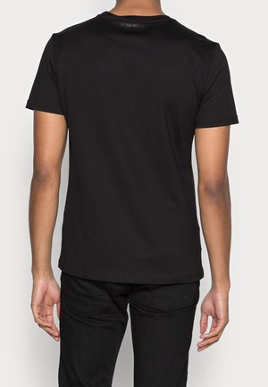 Camiseta negra de manga corta con escote redondo. Hecha de un suave tejido de algodón. Presenta una etiqueta en la parte posterior del cuello.