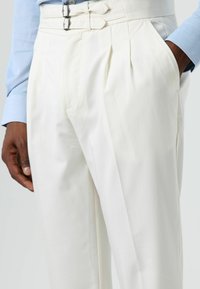 White pleated trousers made of smooth fabric, featuring a double-buckle closure and side pockets. Minimalist design with a tailored fit.