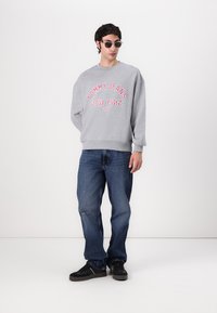 Gray sweatshirt with "TOMMY JEANS NEW YORK CITY" in red graphic, paired with dark blue jeans and black sneakers.