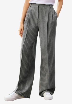 Femme portant un pantalon gris à rayures larges avec des plis, associé à des baskets blanches et un haut blanc rentré.