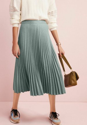 Misia plisowana midi w miękkim turkusowym materiale o fakturowanej powierzchni. Połączona z zieloną torebką i wielokolorowymi butami sportowymi.