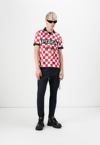 Red and white checkered short-sleeve shirt with black collar and logos, paired with dark cargo pants and black chunky shoes.