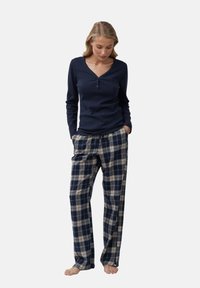 Camisa de manga larga azul marino con escote en V y botón frontal, combinada con pantalones de franela a cuadros en azul marino y crema, con una cinturilla elástica.