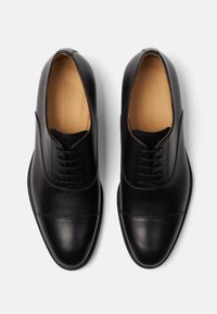 Scarpe eleganti in pelle nera con texture liscia, punta arrotondata, sistema di allacciatura a sei occhielli e dettagli di cucitura delicati sulla tomaia.