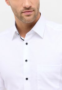 Hvid knap-up skjorte med et mønstret krave, sorte knapper og en brystlomme. Glat stof med en skræddersyet pasform.