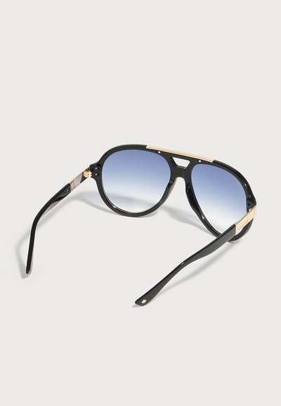 Μαύρα γυαλιά ηλίου aviator με φακούς μπλε διαβάθμισης και χρυσές λεπτομέρειες στο σκελετό και τα μπράτσα, εμφανιζόμενα σε ανοιχτό φόντο.