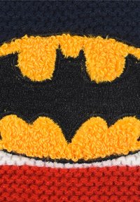 Batman logo on a textured black background, featuring a raised yellow emblem with a wavy edge, complemented by a red lower section.