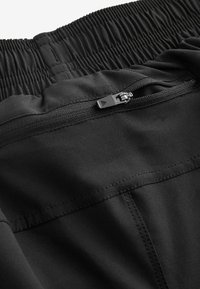 Svarta sportshorts med en rynkad midja, en säker ficka med dragkedja och en mjuk tygtextur med minimala sömdetaljer.