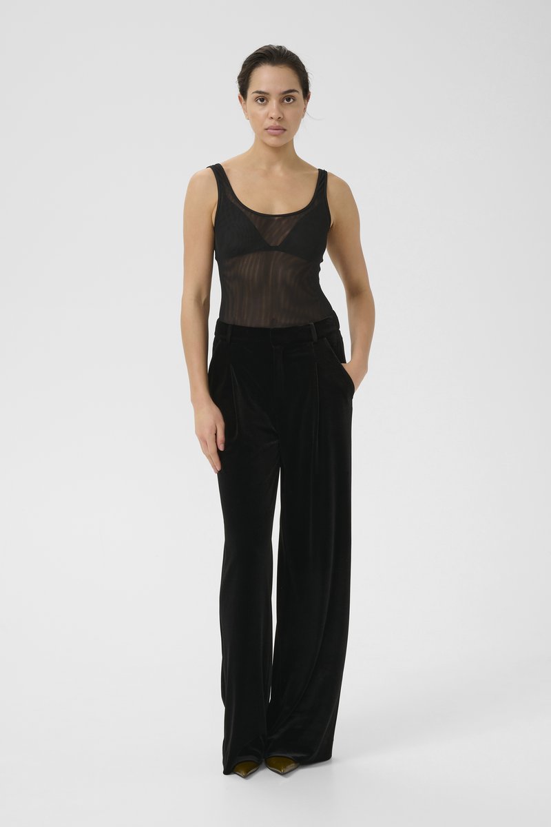 Black sheer bodysuit with vertical stripes, paired with high-waisted black velvet wide-leg trousers and pointed black shoes with green accents.