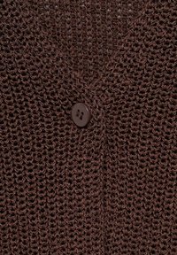 Brązowy sweter o dzianinowej strukturze z dekoltem w kształcie litery V i jednym brązowym guzikiem. Tekstura jest luźno tkana, ukazując otwarty wzór.