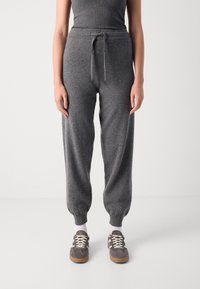 Grå strikkede joggebukser med elastiske mansjetter, snorsnor i midjen og en kosete tekstur, kombinert med grå sneakers og hvite sokker.
