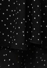 Tessuto nero con pois bianchi, caratterizzato da una superficie liscia e un design drappeggiato. I bordi sono rifiniti in modo pulito senza orli grezzi.