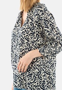 Camicia a maniche lunghe con un motivo a vortice blu navy e crema, caratterizzata da una scollatura a V e polsini con bottoni. Realizzata in tessuto leggero con texture.