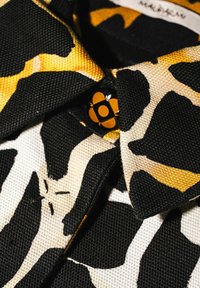 Tessuto con motivo nero, giallo e crema, con un bottone lucido a forma di fiore nero, caratterizzato da una finitura testurizzata e dettagli di cuciture visibili.