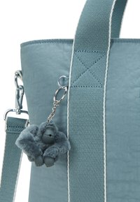 Blue tote bag with wide fabric straps and a small plush gorilla keychain attached to a metal ring.