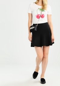 Vit t-shirt med körsbärstryck, svart utsvängd kjol, svart kuvertväska med blommig dekoration och svarta slip-on-skor med ulldetaljer.