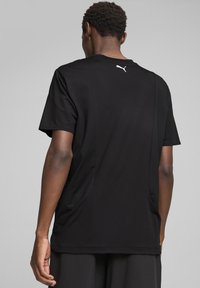 Sort kortærmet træningsshirt lavet af glat stof, med et hvidt logo på ryggen og et simpelt, strømlinet design.