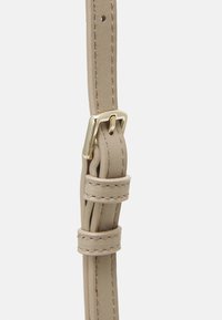 Primo piano di una cintura in pelle beige con cuciture beige e una fibbia rettangolare dorata fissata in un foro perforato.