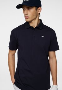 Marinblå polo skjorta med krage, tre knappar och en liten logotyp på bröstet. Kortärmad med en mjuk yta.