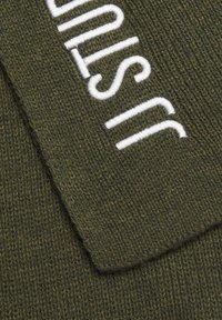 Green knitted scarf featuring white embroidered text. The fabric has a textured finish, showcasing a ribbed pattern throughout.