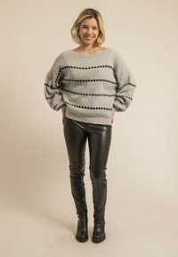 Un pull en maille gris clair avec des rayures horizontales noires, associé à un pantalon en simili cuir noir brillant et des bottines noires.